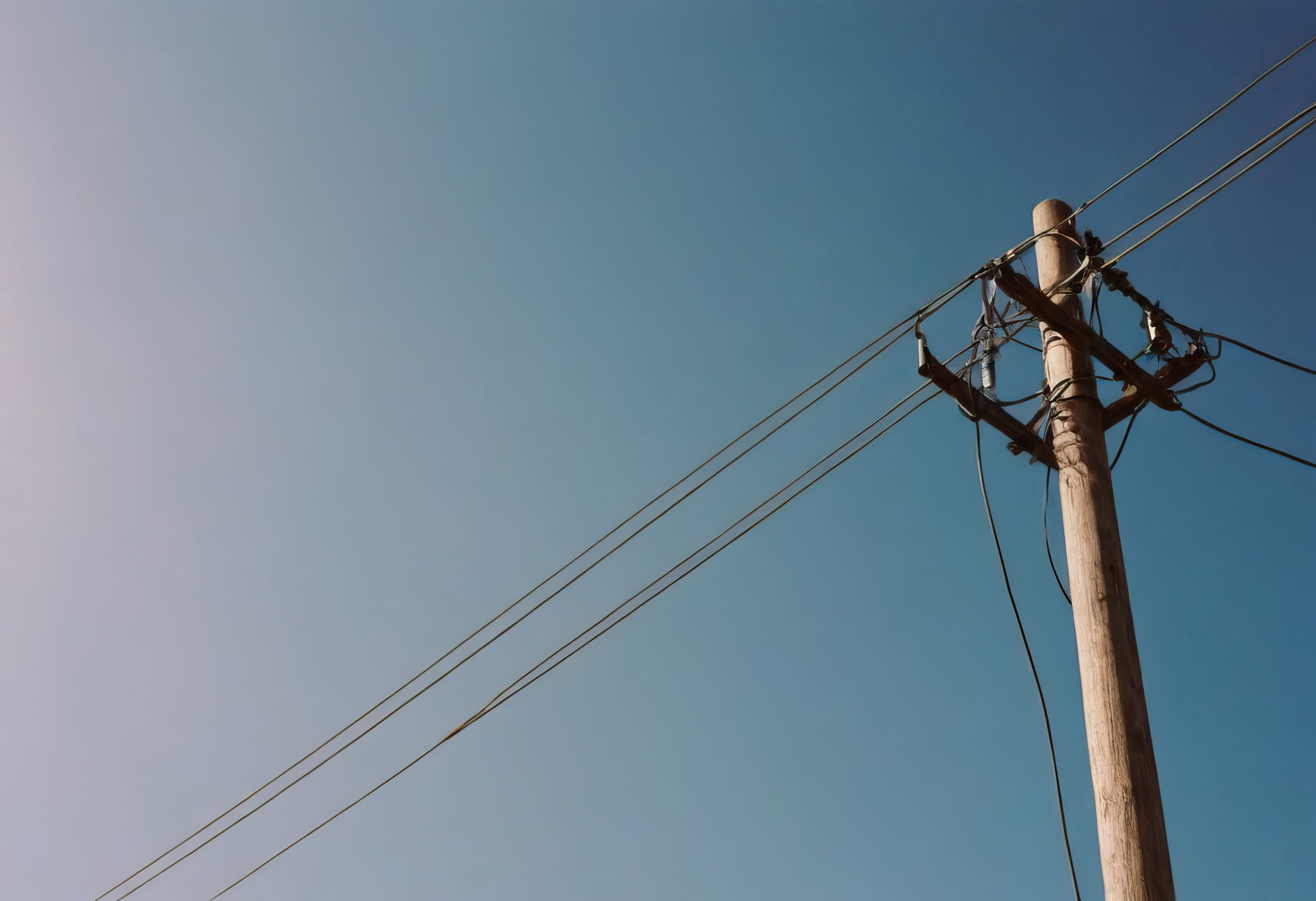 Electrical utility pole with overhead power lines against a clear blue sky.